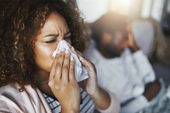 Sick woman, sneeze and blowing nose with tissue on sofa for allergy, virus or flu and cold together at home. Couple, man or female person with influenza for sinus, symptoms or fever season at house