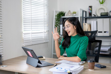 Asian businesswoman making ok sign while video calling on tablet in office