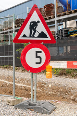 Construction site with gravel road, a speed limit sign with 5km/h and a sign signalling the...