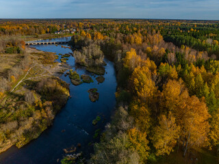 Fototapeta premium Aerial photo of beautiful autumn landscape. Jagala (Estonian Jägala) river meandering through a dense forest of mixed trees - in gold, orange and green colors. Small bridge crosses the river. 