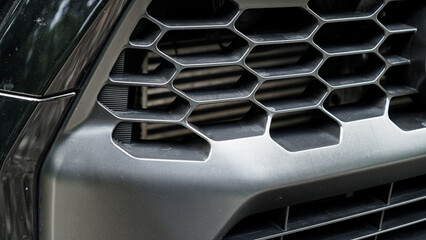 car's front grille, showcasing a hexagonal mesh pattern. The dark, metallic finish and intricate...