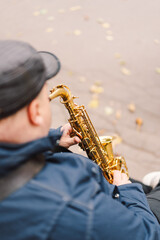 Naklejka premium A saxophonist performs in a serene park during autumn while seated on a bench surrounded by fallen leaves