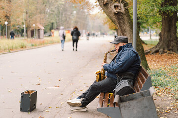 A saxophonist performs in a serene park during autumn while seated on a bench surrounded by fallen leaves