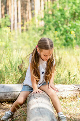 a child, a teenager climbed a tree in the forest, sits, rests alone. joyful little girl sits on a log in the park, in nature, in summer.