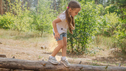 child balancing on a tree trunk during an outdoor adventure. Girl exploring nature walk on a log, while kid enjoy nature while walking outside. Active child walking through log forest