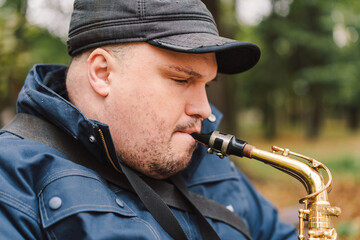 A saxophonist performs in a serene park during autumn while seated on a bench surrounded by fallen...