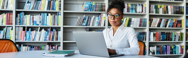 A committed teacher focuses intently on her laptop, surrounded by books in a quiet library.