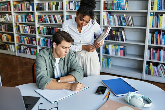 A devoted teacher helps her student with studies amidst shelves of books in a warm environment.