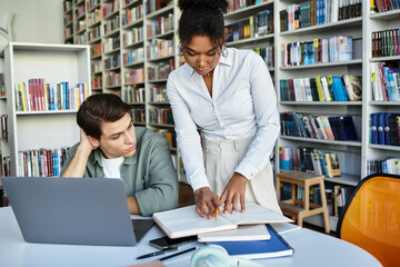 A caring teacher assists a curious student with homework in an inviting library environment.