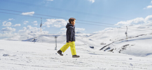 Boy in winter clothes walking on a mountain with snow