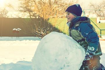 boy sculpt a snowman in the backyard of the house clear winter day. The boy rolls a snowball to build a snowman in the yard during a heavy snowfall. toned.