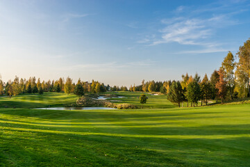 The relief of the golf course with green grass, small ponds, against the background of the .autumn blue sky.