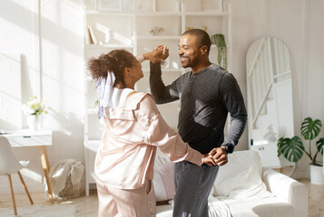 Happy african American young couple relax in kitchen dancing waltzing together at home, overjoyed...