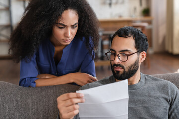 Budget Planning. Stressed thoughtful mixed race couple spouses holding papers and calculating...