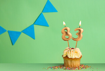 Birthday cupcake with number 83 candle - Green background with blue pennants.
