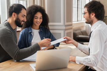 Focused married couple signing document, insurance agreement, closing real estate deal at meeting...
