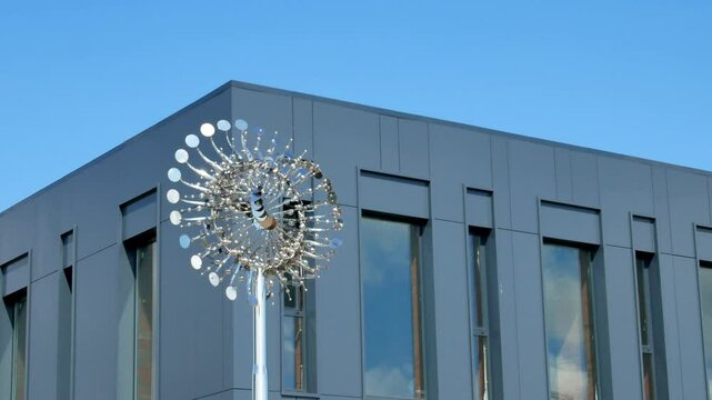 An innovative weather vane made of mirrored circles fascinatingly beautifully rotate in the wind, move back and forth, change direction against the background of a modern gray building.