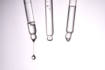 Three pipettes with a cosmetic product. Serum or fluid drips from one of them.