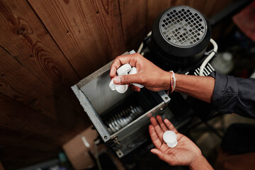 Hands of unrecognizable male worker putting white plastic bottle caps into processing machine in factory or workshop
