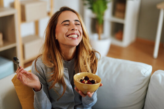 Happy woman enjoying healthy breakfast with oatmeal and berries at home