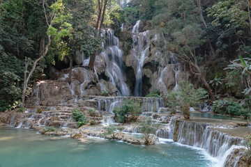 Kuang Si waterfall in Luang Prabang, Laos, flows into a Turquoise water with a lush green forest in the background.