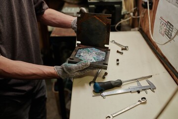 Hands of unrecognizable male technician in protective gloves opening metal press mold with multicolor polymer tile