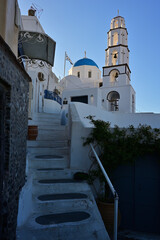 Eine Treppe führt auf einer Griechischen Insel zur einer Kirche und die Häuser haben die typischen weiße Hausfassaden, die einen schönen Kontrast zum strahlend blauen Himmel bilden.