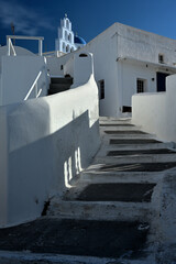 Eine Treppe führt auf einer Griechischen Insel zur einer Kirche und die Häuser haben die typischen weiße Hausfassaden, die einen schönen Kontrast zum strahlend blauen Himmel bilden.