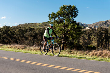 Fototapeta premium Male cyclist riding his bike in the middle of a road with a background of forests and mountains outdoors 