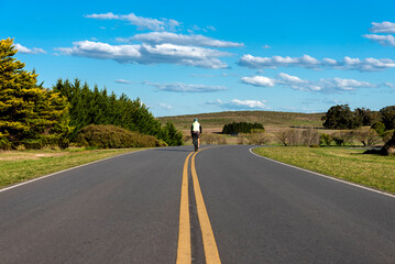 Male cyclist riding his bike in the middle of a road with a background of forests and mountains outdoors  