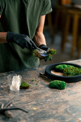 close up hands in large green workshop a thin woman with green hair in black gloves at a large...