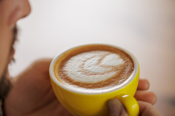 Man enjoying a cup of coffee on a break from work. Close-up of a handsome man, with a yellow cup of coffee in his hands. Moments of enjoying and relaxing.