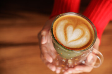 Hands of a woman holding a cup of coffee. Latte art, heart drawn in coffee, caffeine for energy. Customer, student or businessman having breakfast in a store or cafe.