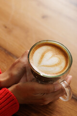 Hands of a woman holding a cup of coffee. Latte art, heart drawn in coffee, caffeine for energy. Customer, student or businessman having breakfast in a store or cafe.