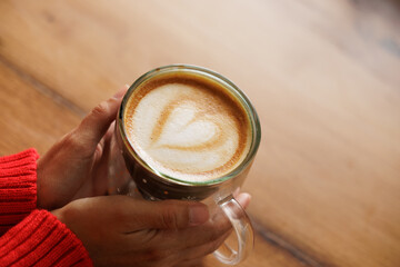 Hands of a woman holding a cup of coffee. Latte art, heart drawn in coffee, caffeine for energy. Customer, student or businessman having breakfast in a store or cafe.