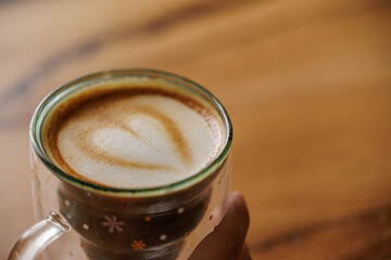 Hands of unrecognizable woman in red sweater sitting at table enjoying specialty coffee in cafe with Christmas mug with star drawings.