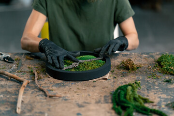 close up hands in large green workshop a thin woman with green hair in black gloves at a large...