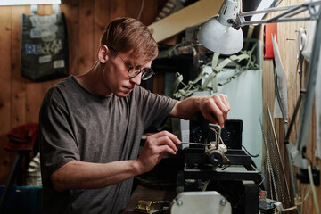 Young professional technician of recycling workshop bending over metalwork machine while fixing small details