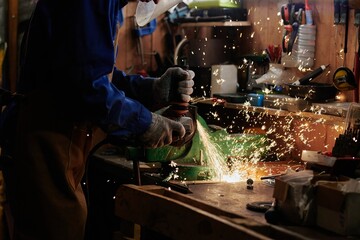 Hands of unrecognizable metalworker in protective mask and gloves grinding metal detail of industrial machine