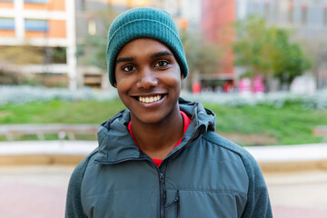 Happy young African American man smiling at camera in winter city, wearing warm clothes, exuding confidence and happiness. Portrait of Gen Z black boy at city street