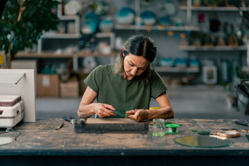 in large green workshop, a thin woman with green hair at a large table cuts out green petals from...