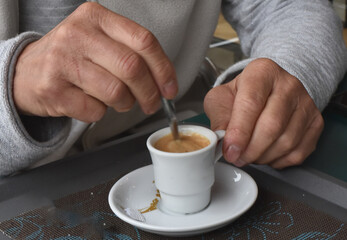the hands of an old man hold a spoon and a cup of coffee