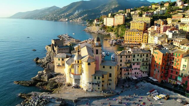 Camogli, a charming fishing village on Italy's Ligurian coast, captured from the air at sunset, reveals its colorful houses and historic harbor bathed in a warm, golden light