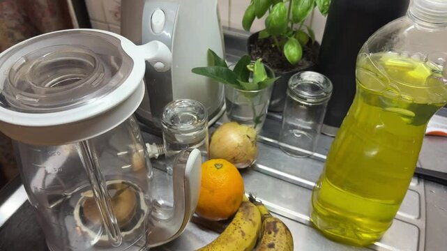 A completely messy kitchen countertop, with fruits, glasses, plants, and containers