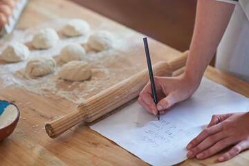 hands, baking and writing a recipe in kitchen for dough preparation, checking steps and...