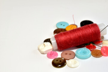 A spool of red thread, needles and buttons lie on the seamstress's table.
