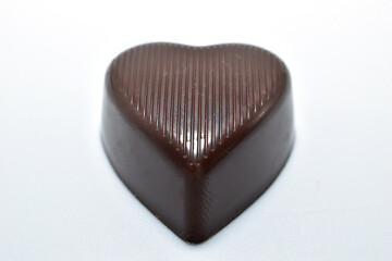 A chocolate heart-shaped candy lies on a white background.