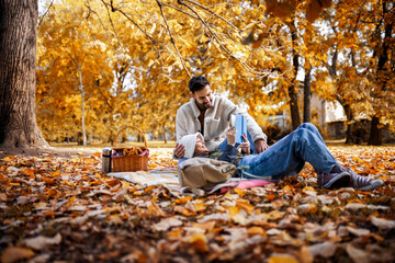 Young cute couple has picnic and reads book together in an colorful autumn park.