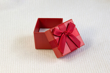 Closed red gift box with silk red ribbon bow on white knitted background
