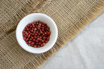 Red or pink peppercorns on wooden spoon on grey textured linen background